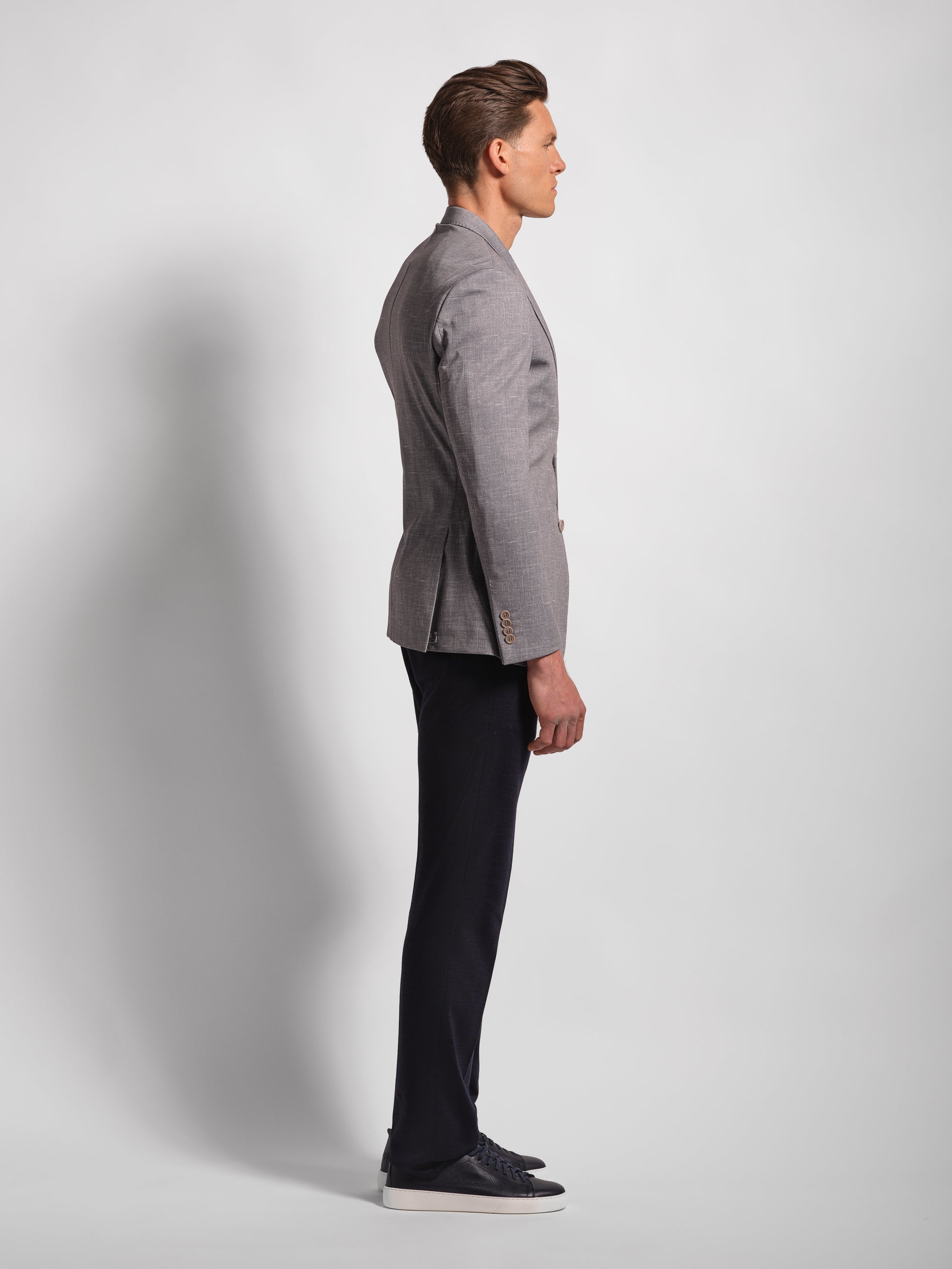 Man wearing a gray stretch jersey blazer profile and Navy pants against a white background,
