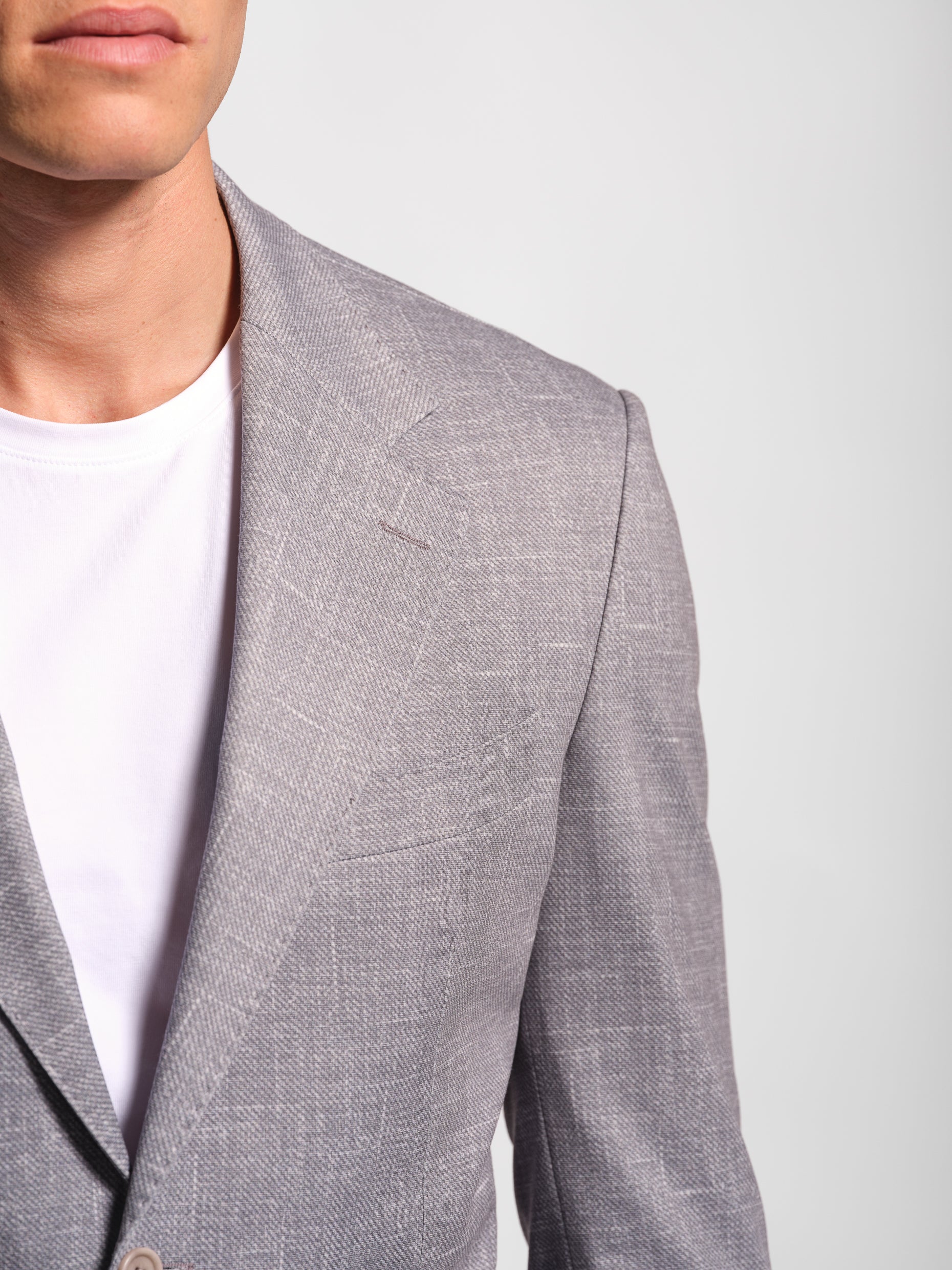 Gray blazer over a white shirt on a plain background with top stich and barcatta pocket