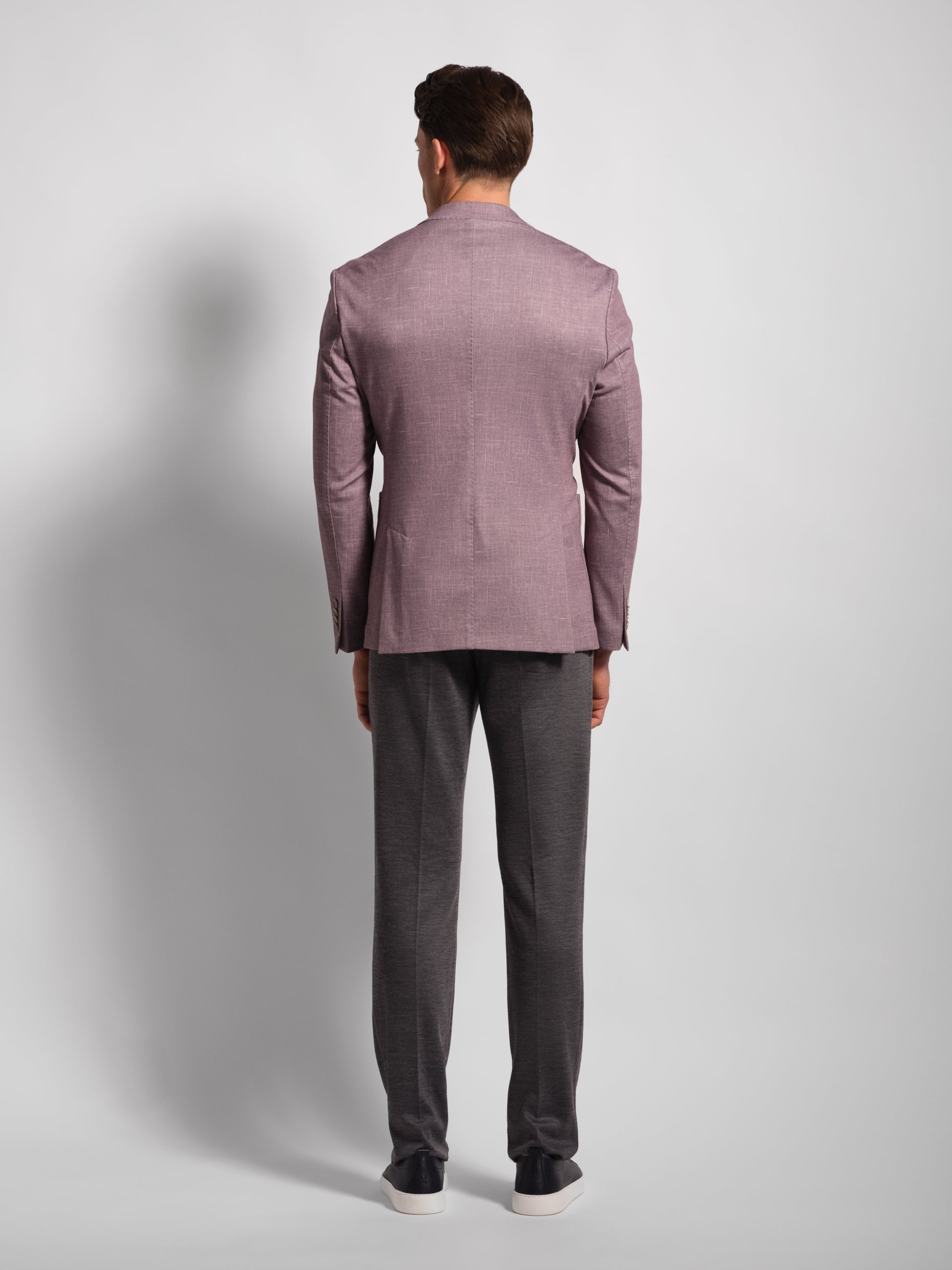 Back of Man wearing a purple blazer and gray pants on a light gray background