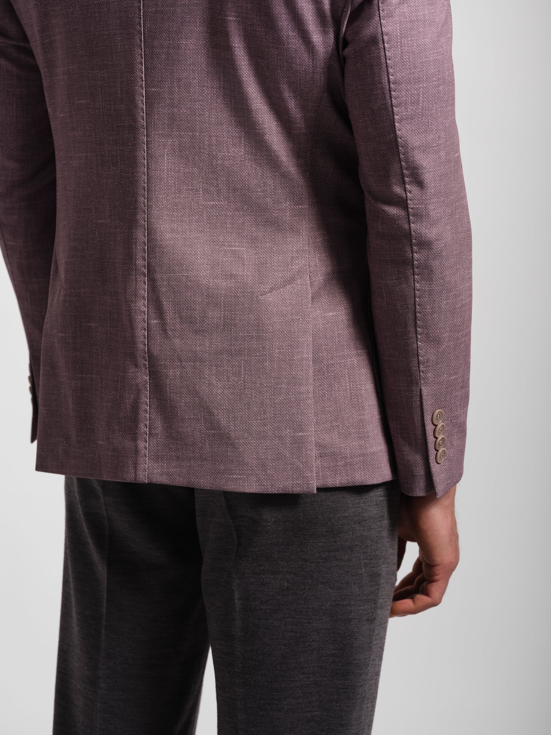 Close-up of a person wearing a comfortable mauve blazer silver suit jacket and gray pants on a light gray background