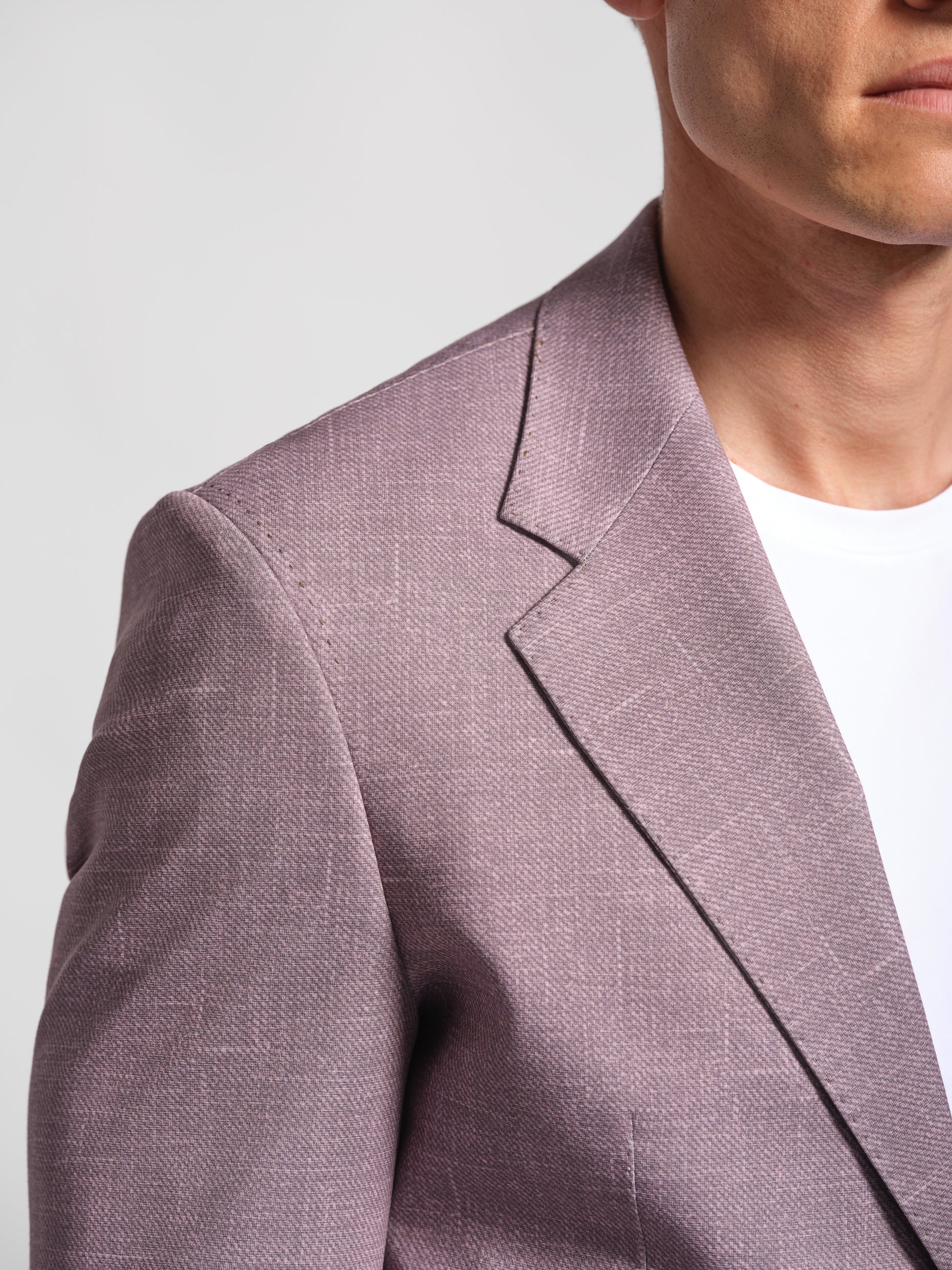 Close-up of a person wearing a light purple wide lapel comfortable blazer top stich detail against a plain background