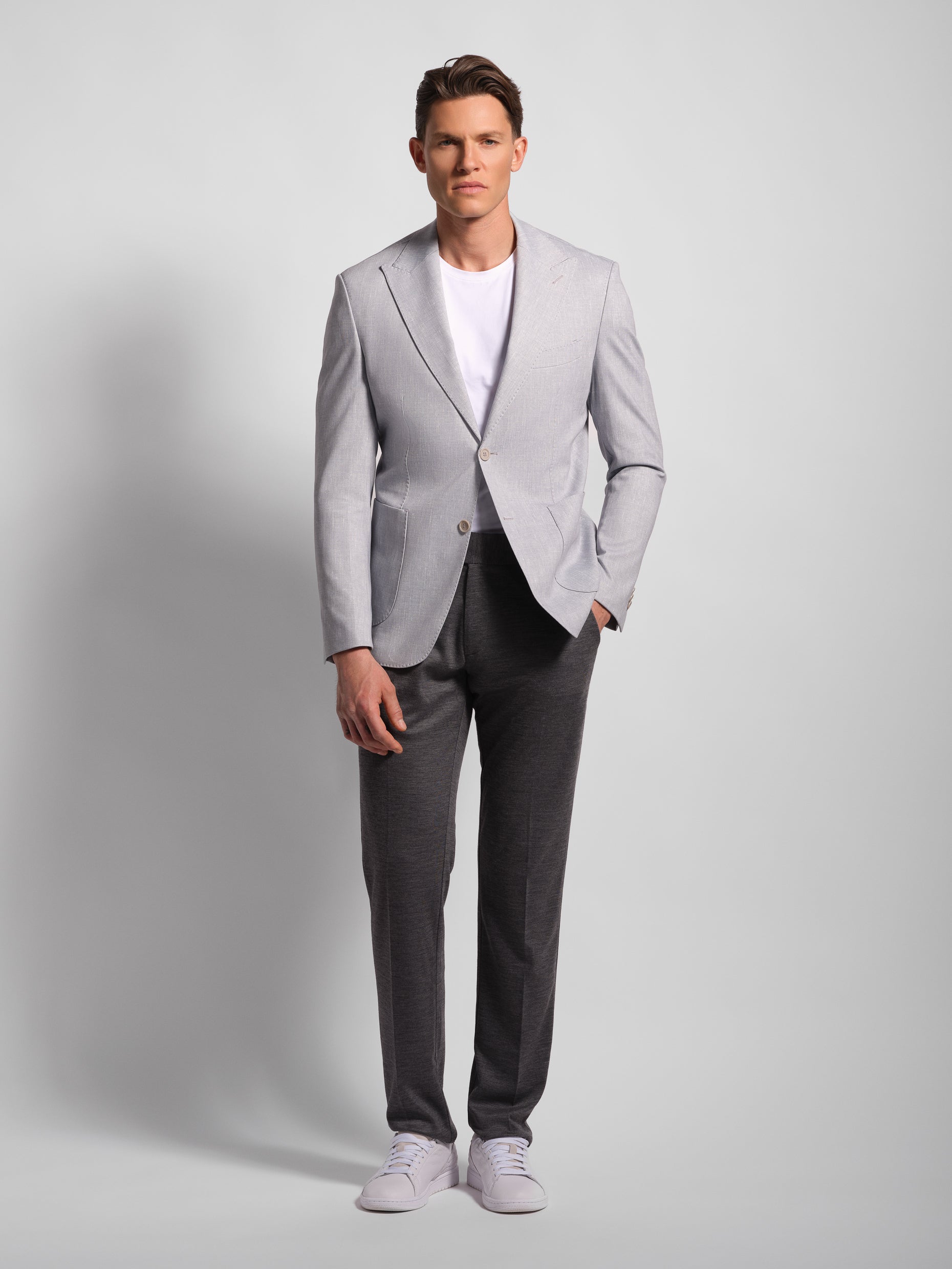 Man wearing a light gray a stretch and comfortable jacket blazer, white shirt, and dark gray pants on a plain background