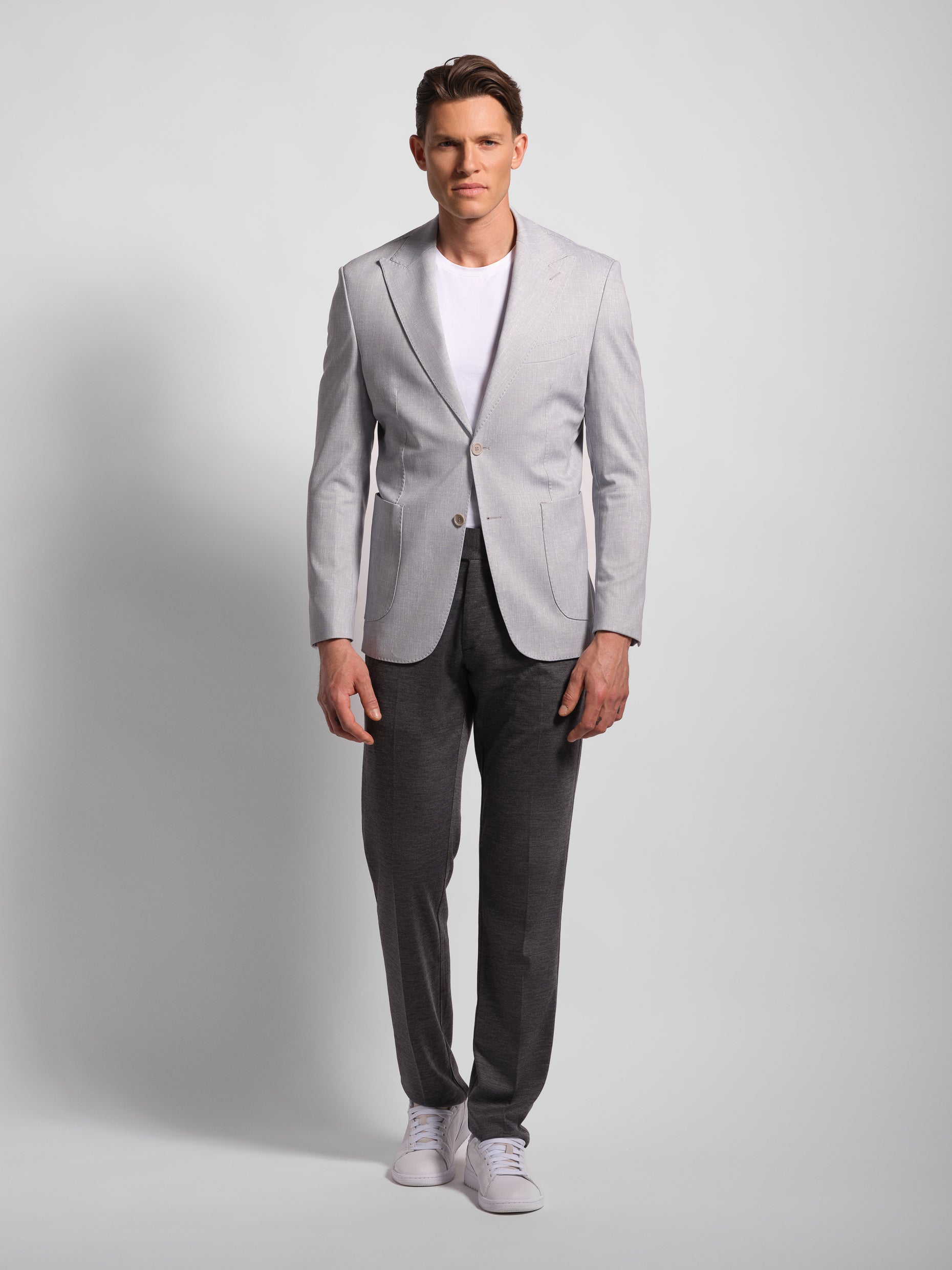 Man wearing a light gray blazer over a white shirt with dark pants on a and patch pockets