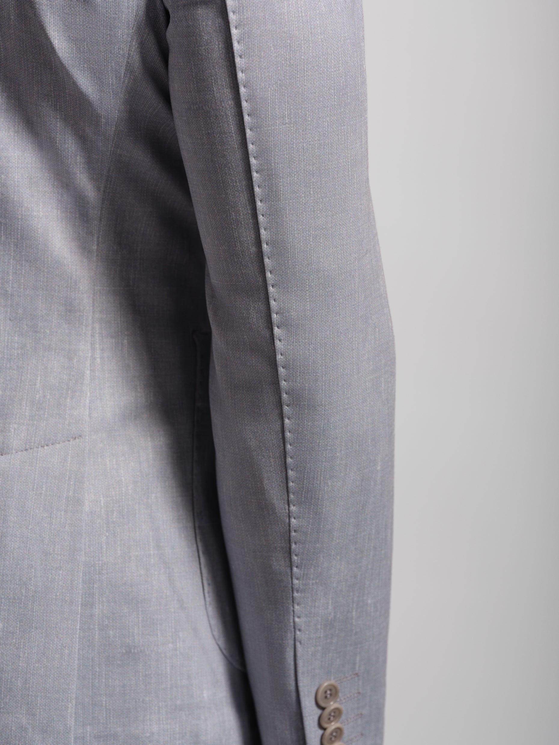 Close-up of a gray suit jacket with a button and top stiching on a light gray background