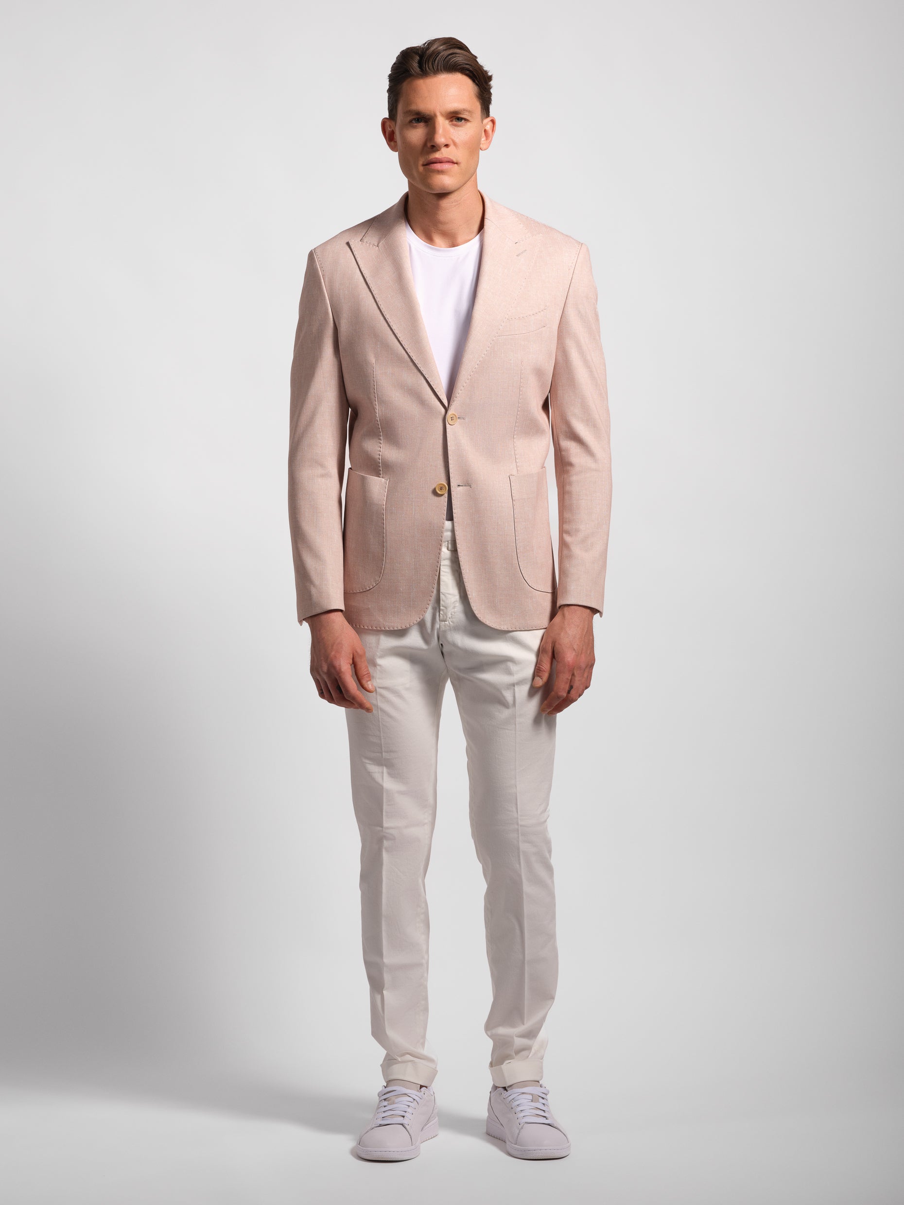 Man wearing a light pink blazer over a white shirt and white pants on a white background stretch jacket