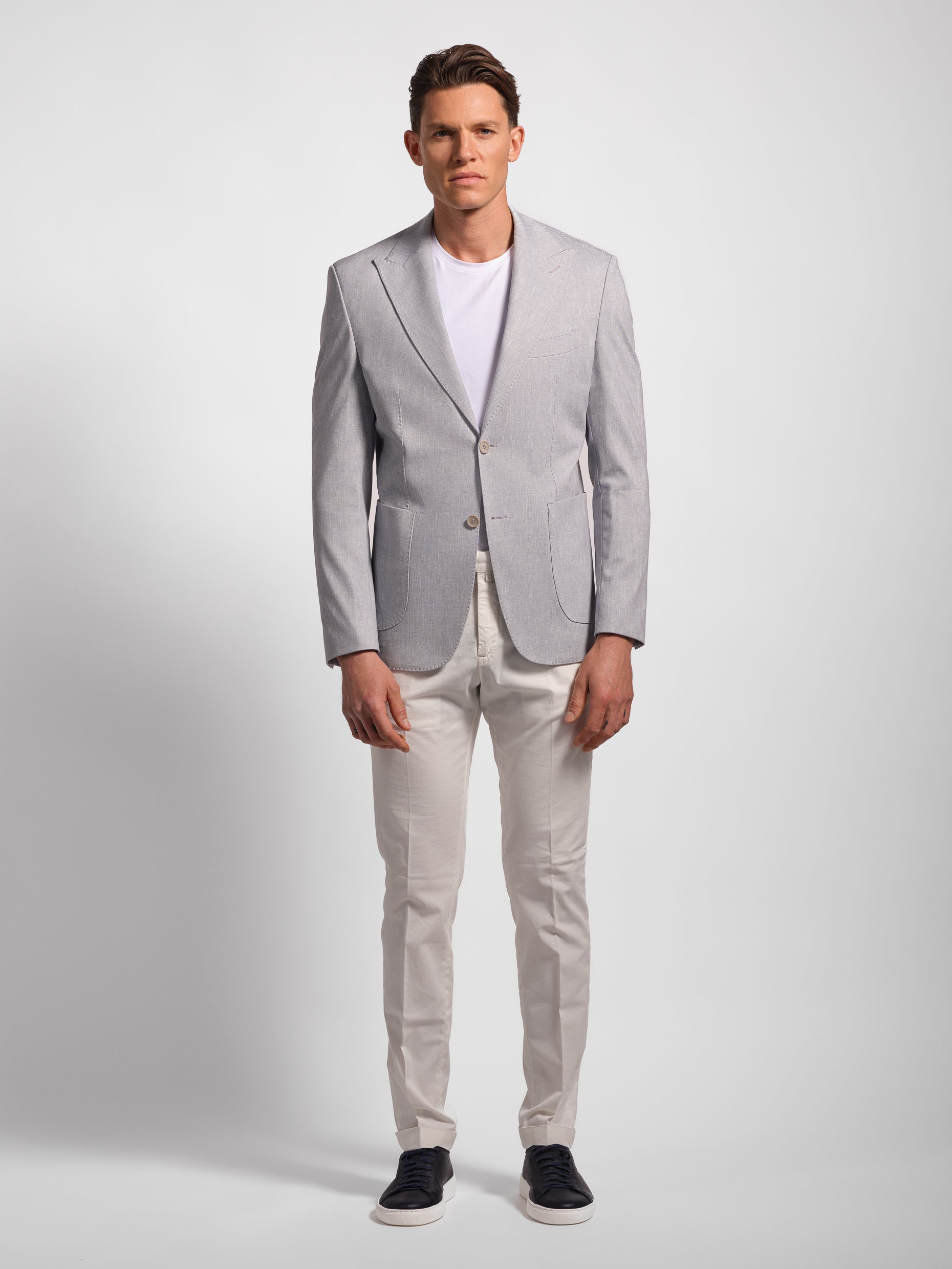 Man wearing a gray blazer, white shirt, and white pants on a light gray background with peak lapel