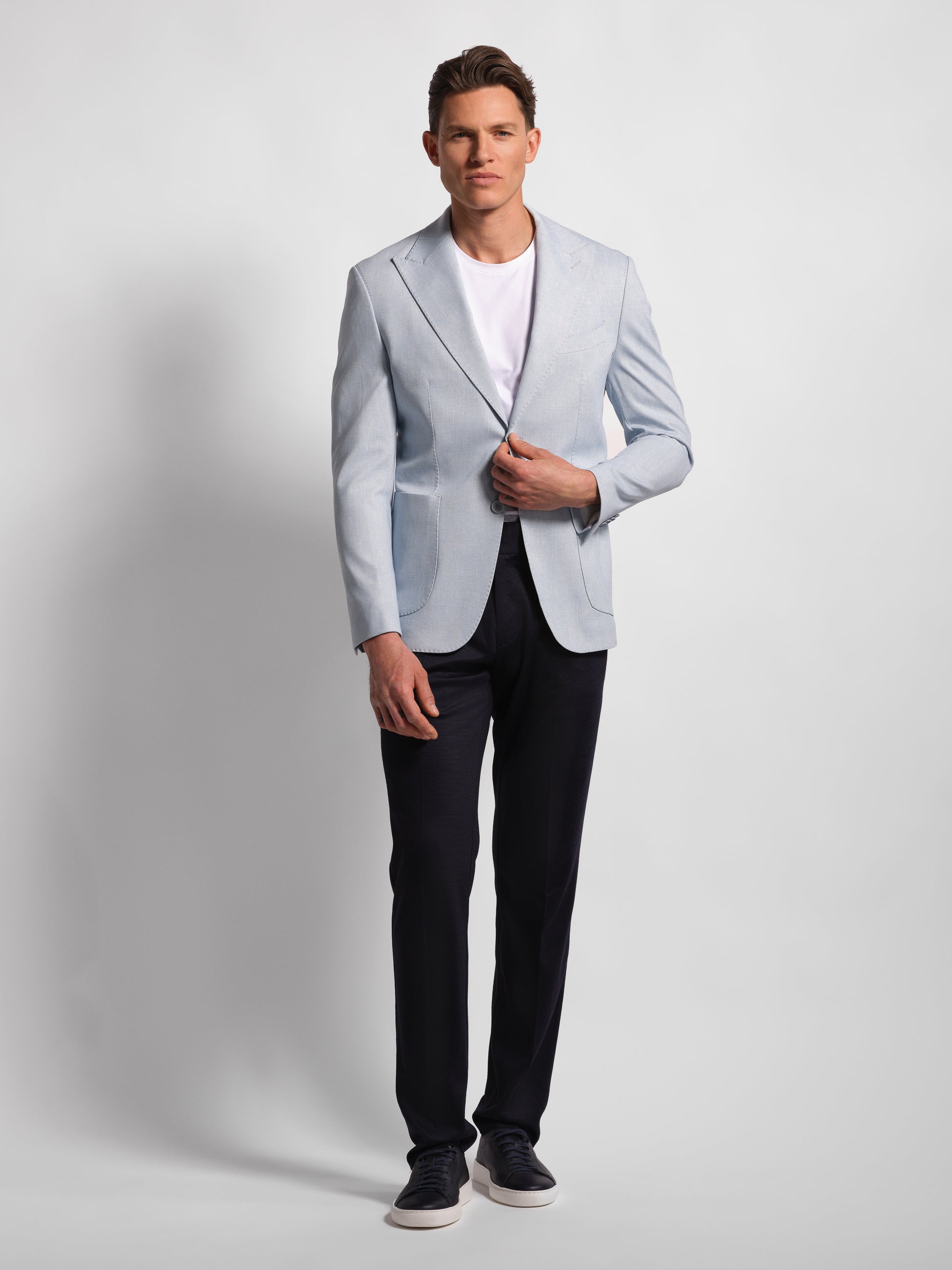 Man wearing a light Blue blazer over a white shirt with Navy pants on a plain background