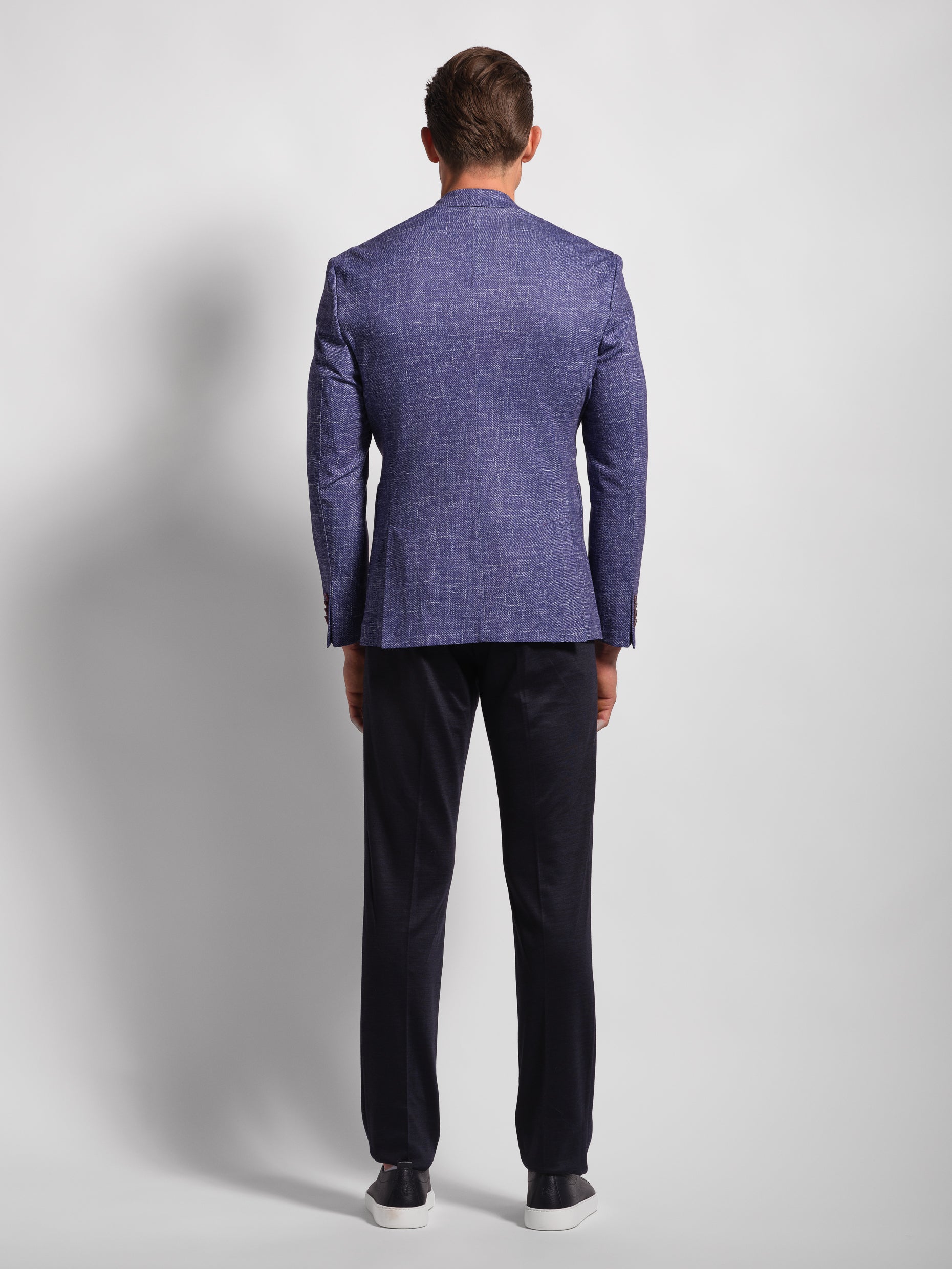 back of man wearing a stretch jersey purple blazer over a white shirt and Navy pants with wide notch lapels and patch pockets model