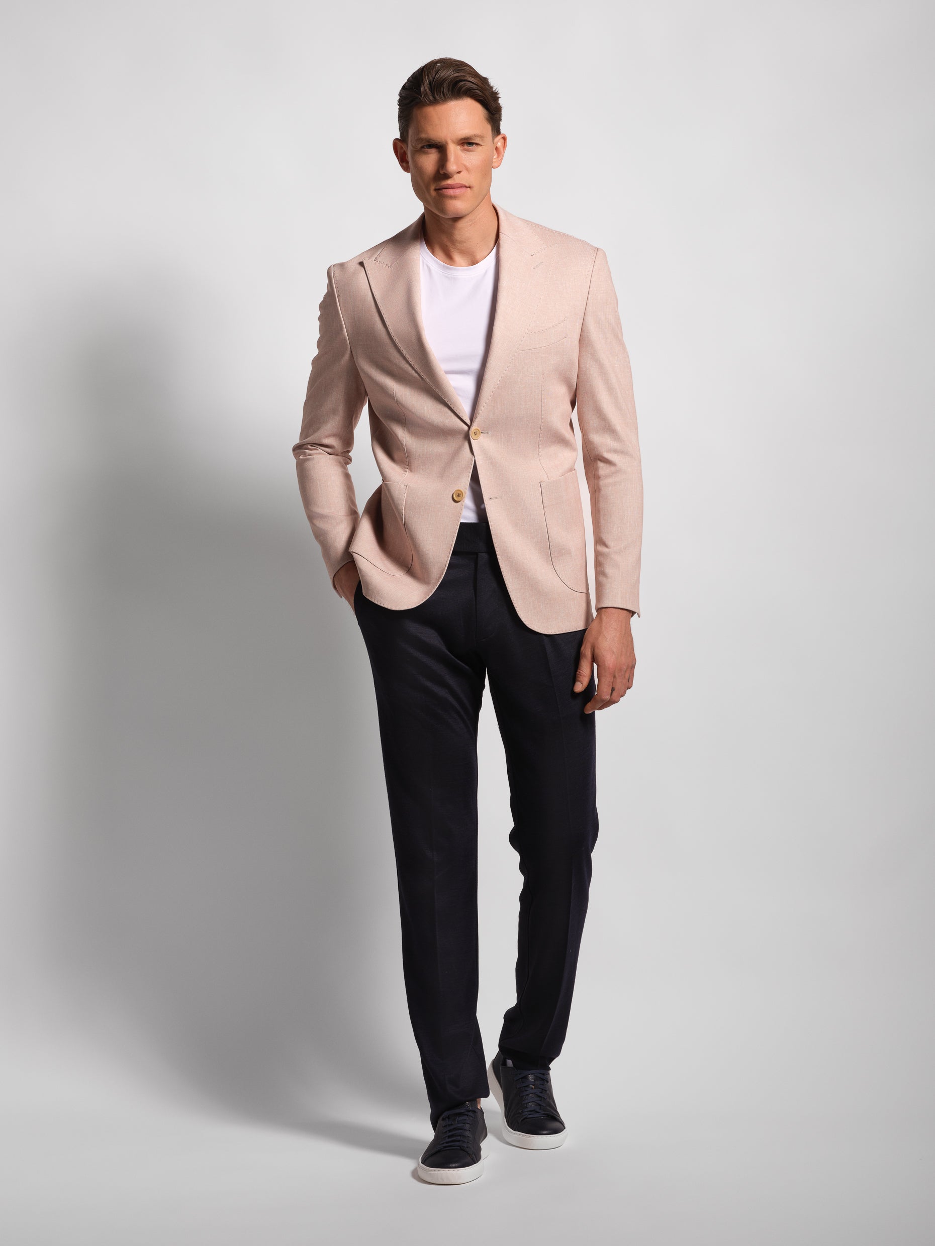 Man wearing a light coral blazer, white shirt, and black pants on a gray background with peak lapel