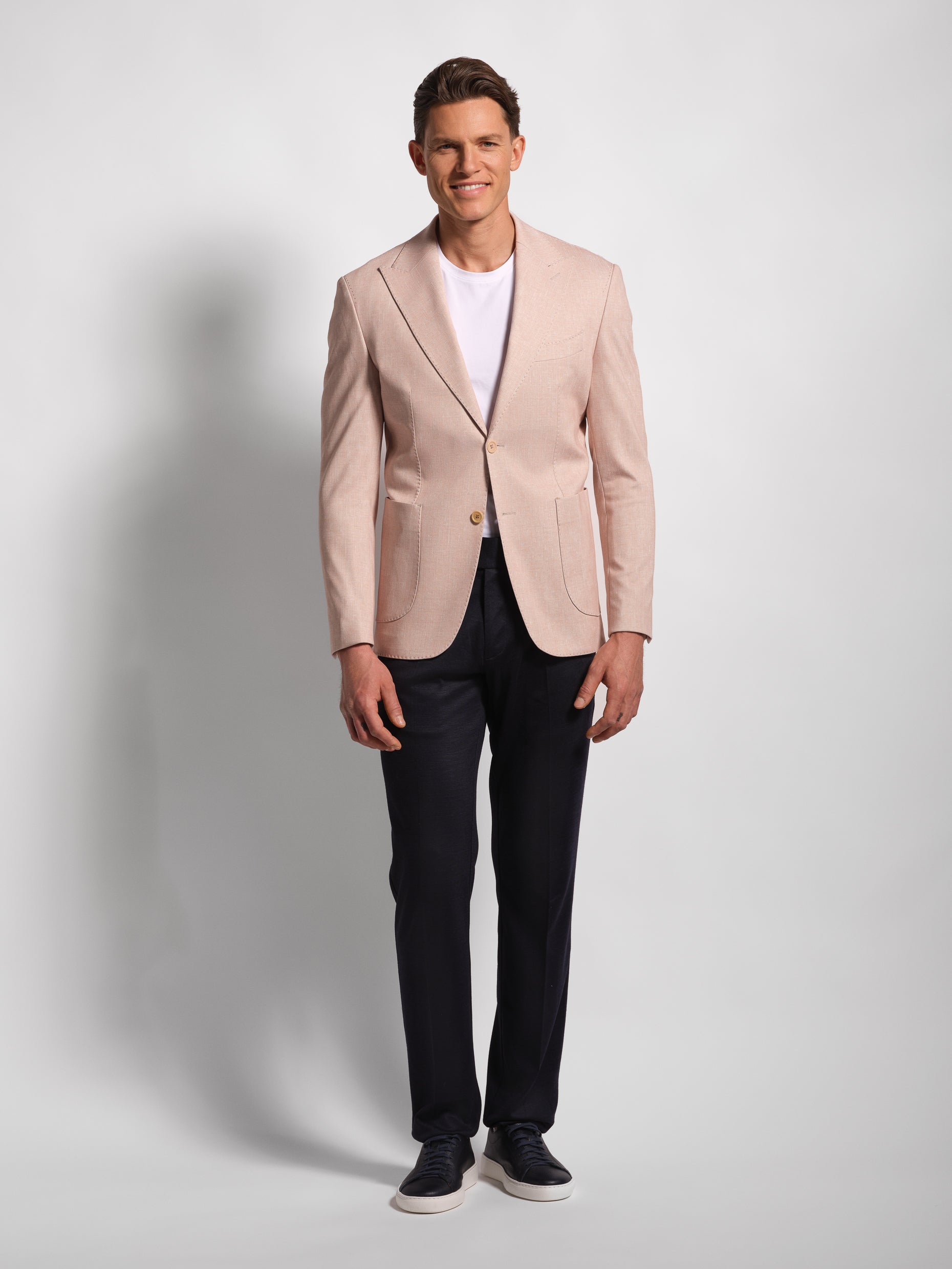 Man wearing a light pink blazer over a white shirt with dark pants on a plain background in stretch and comfortable