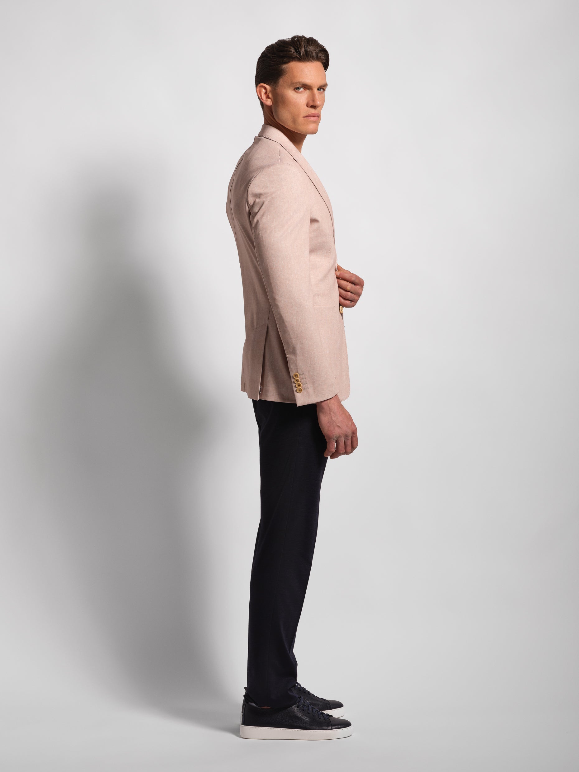 Man wearing a beige blazer and black pants on a light gray background with side profile in a stretch and comfortable jacket