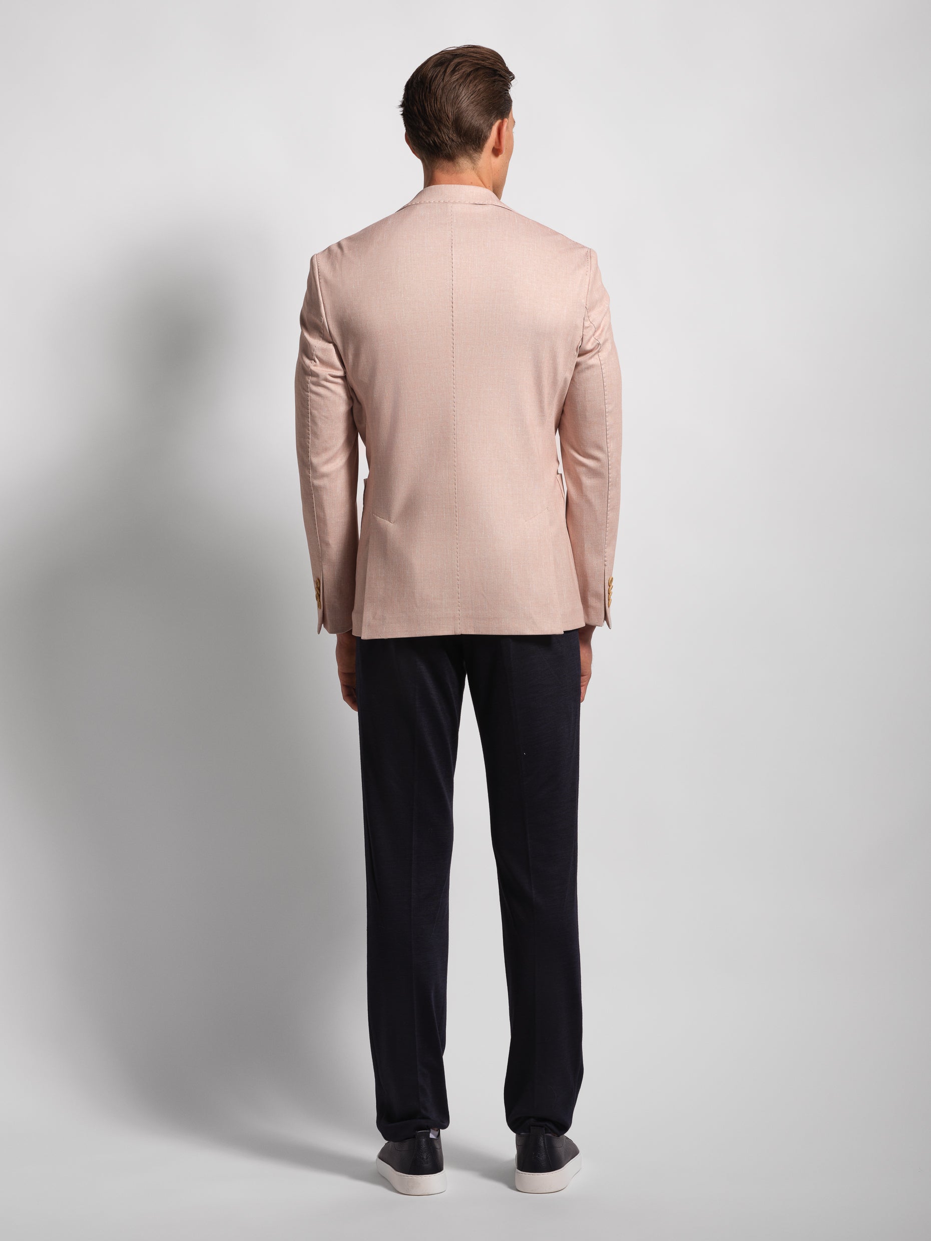 Back of Man wearing a coral blazer and navy pants on a light gray background double vents