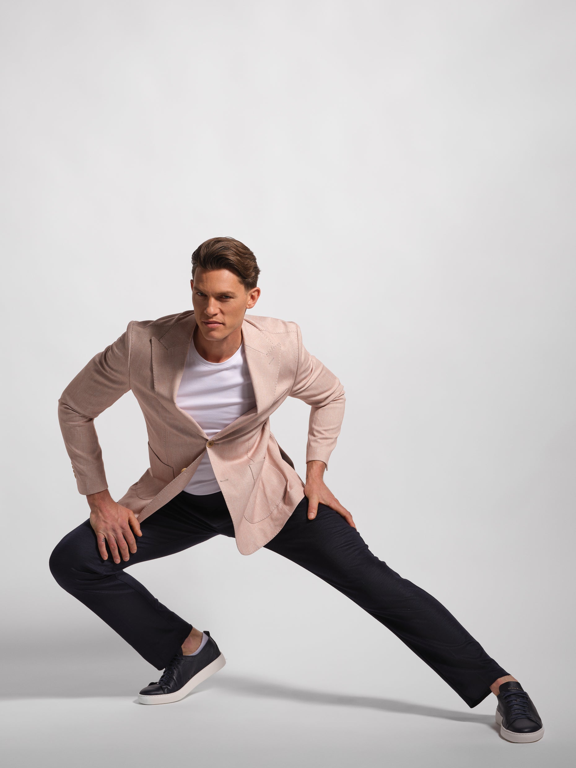 Man posing in a stylish outfit with a coral jacket, white shirt, and black pants on a light gray background, showing a stretch and comfortable jacket