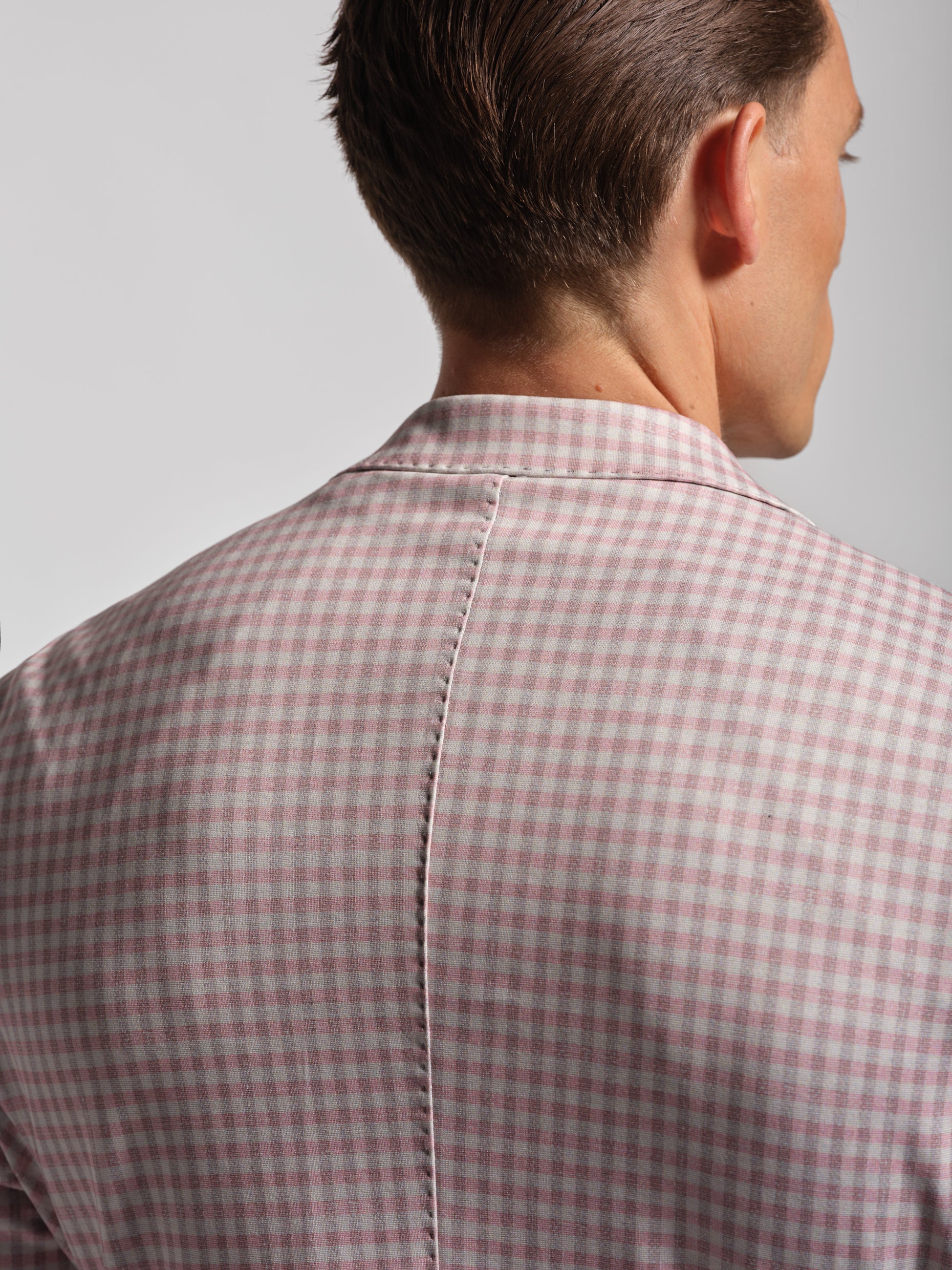 back of man wearing a red and white checkered shirt against a gray background