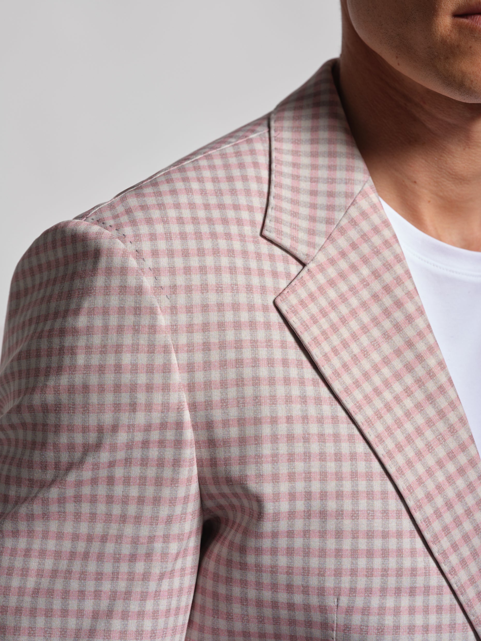 Close-up of a person wearing a pink and gray checkered blazer over a white shirt.