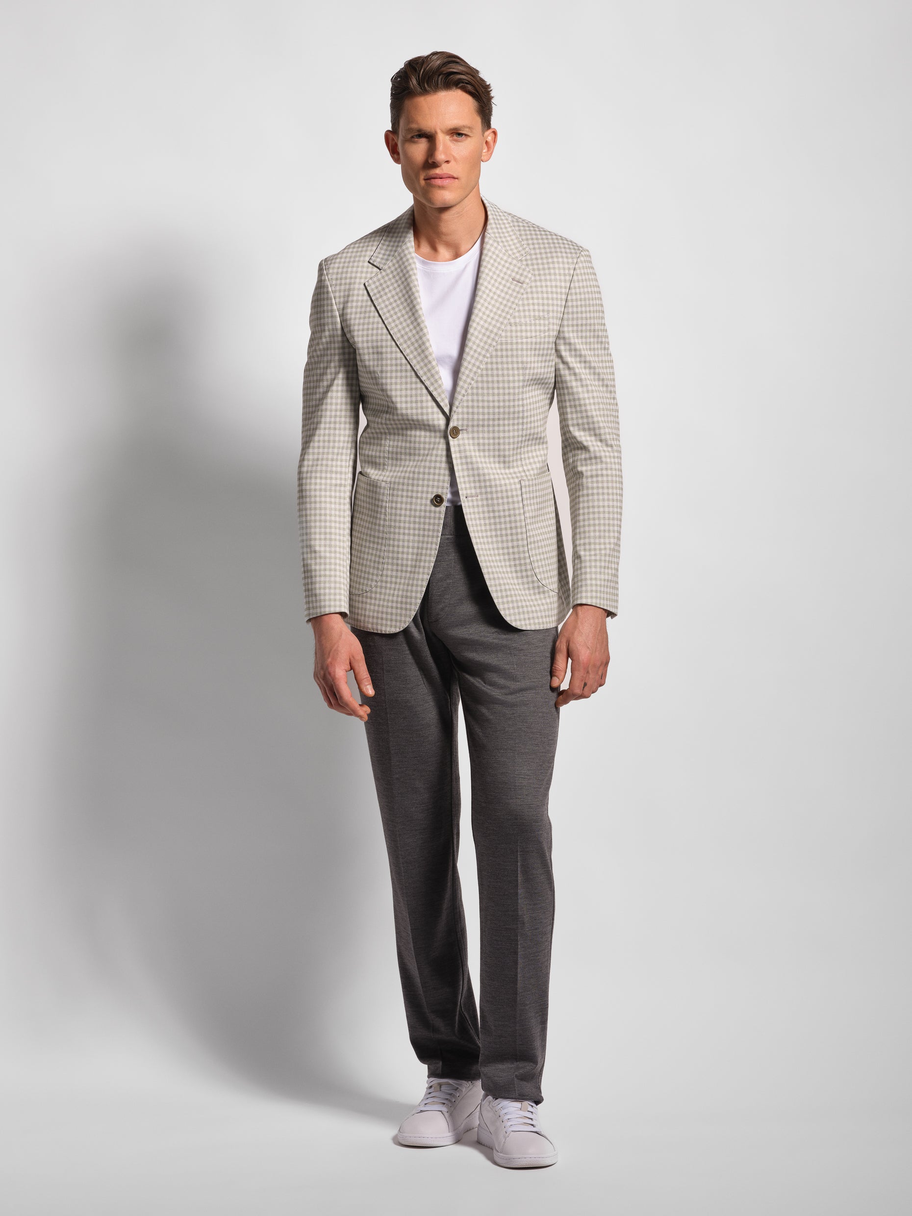 Man wearing a checkered blazer over a white shirt with gray pants on a light gray background