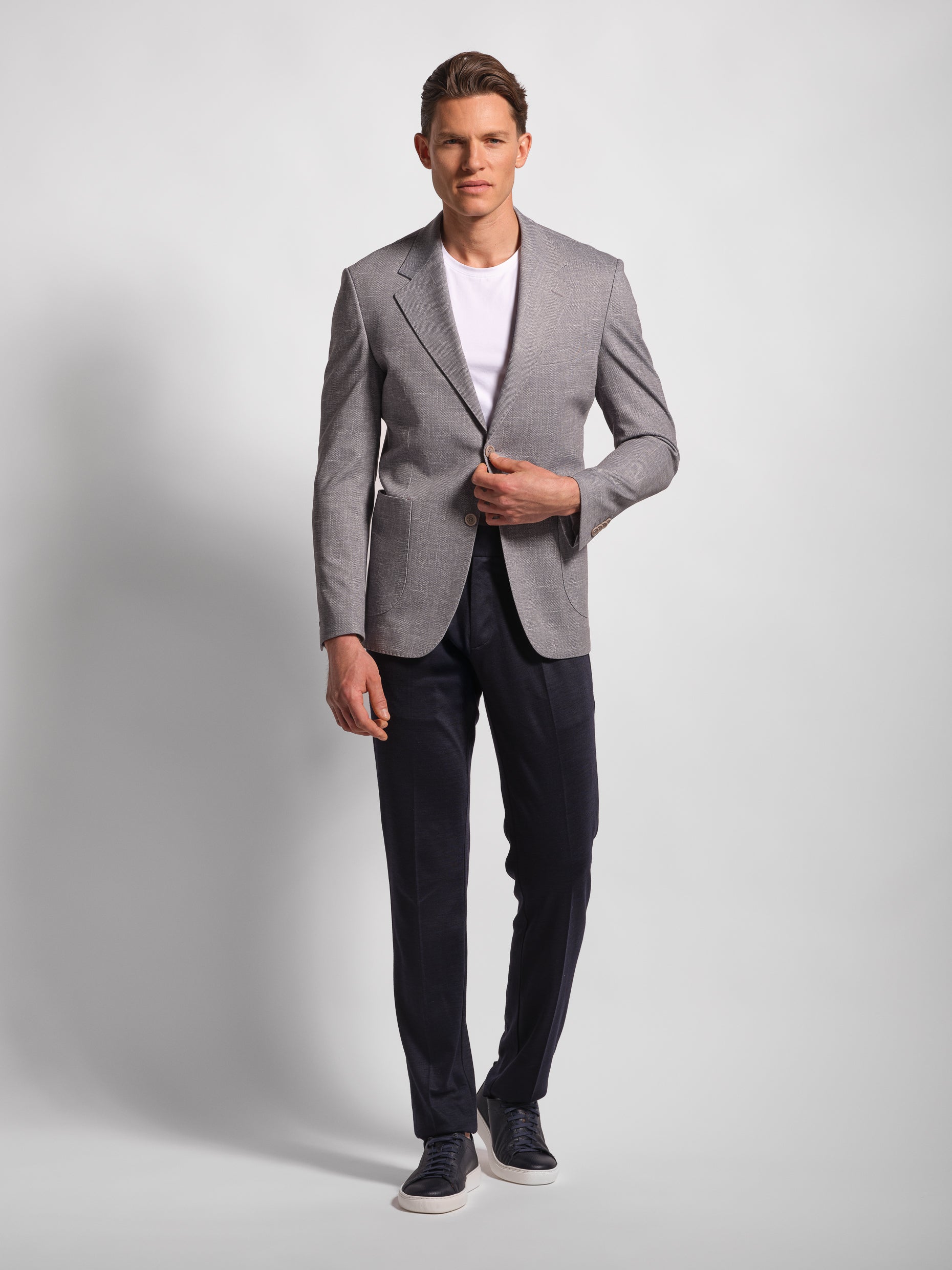 Man wearing a gray blazer and navy pants on a light gray background