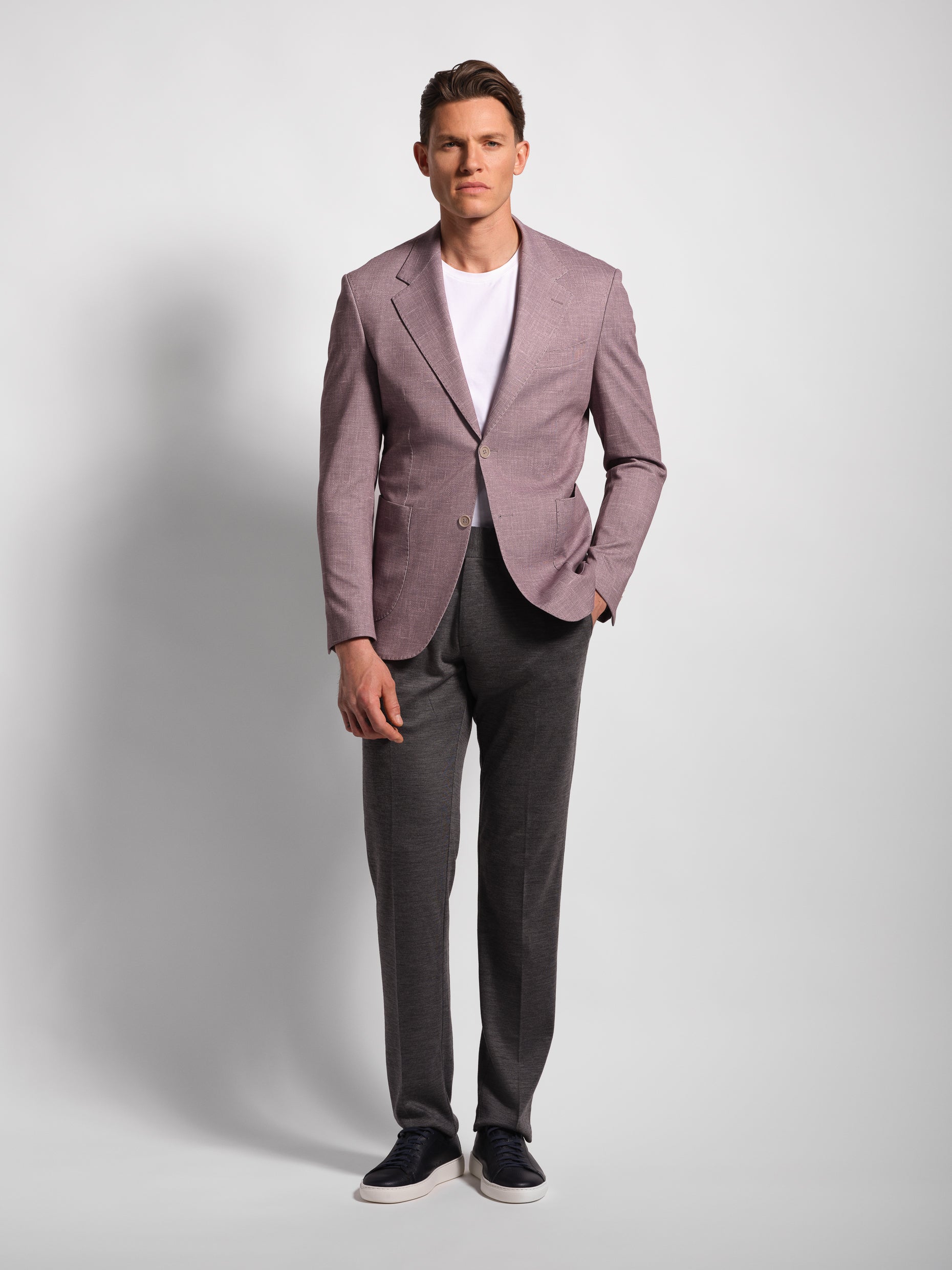 Man wearing a light purple comfortable blazer over a white shirt with gray pants on a plain background