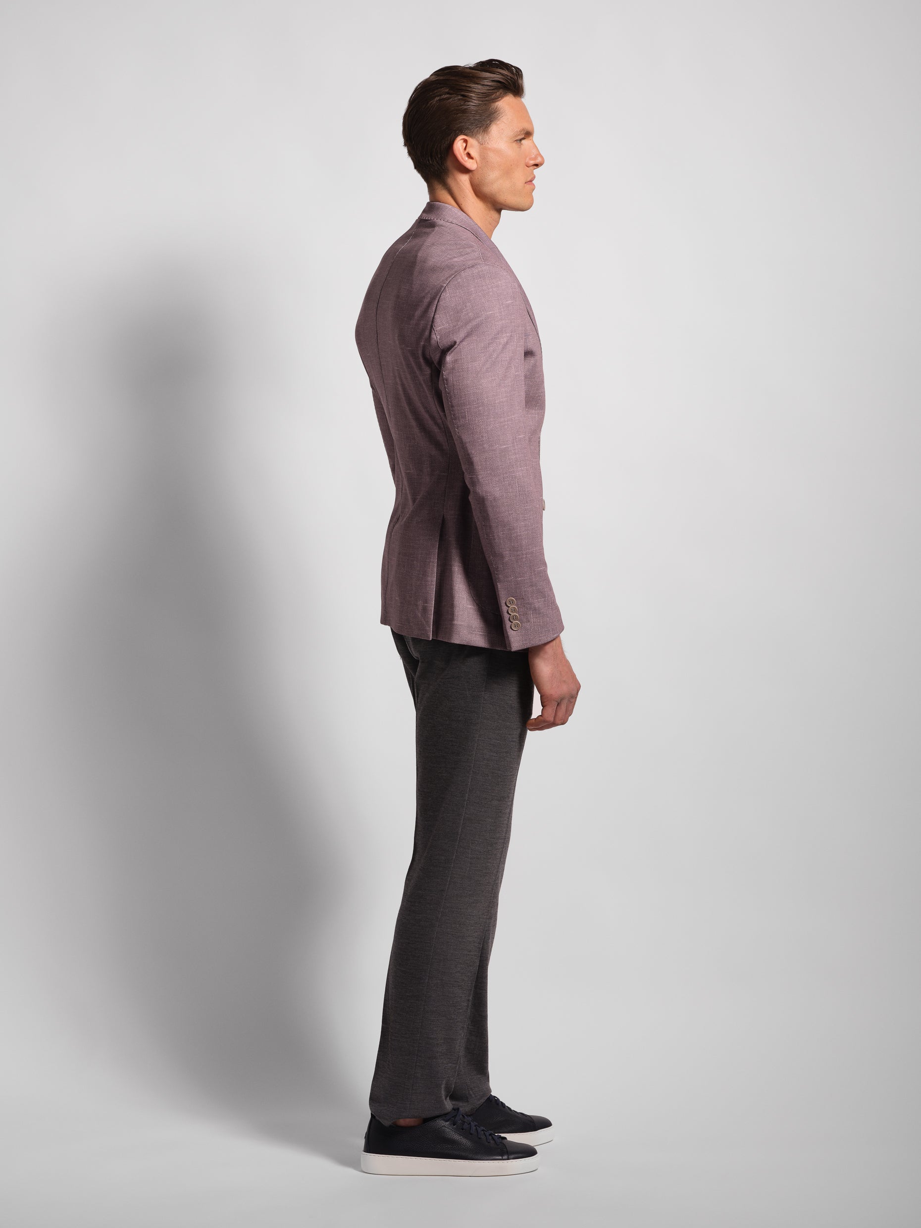 Man wearing a mauve blazer comfortable blazer side view and dark pants on a light gray background