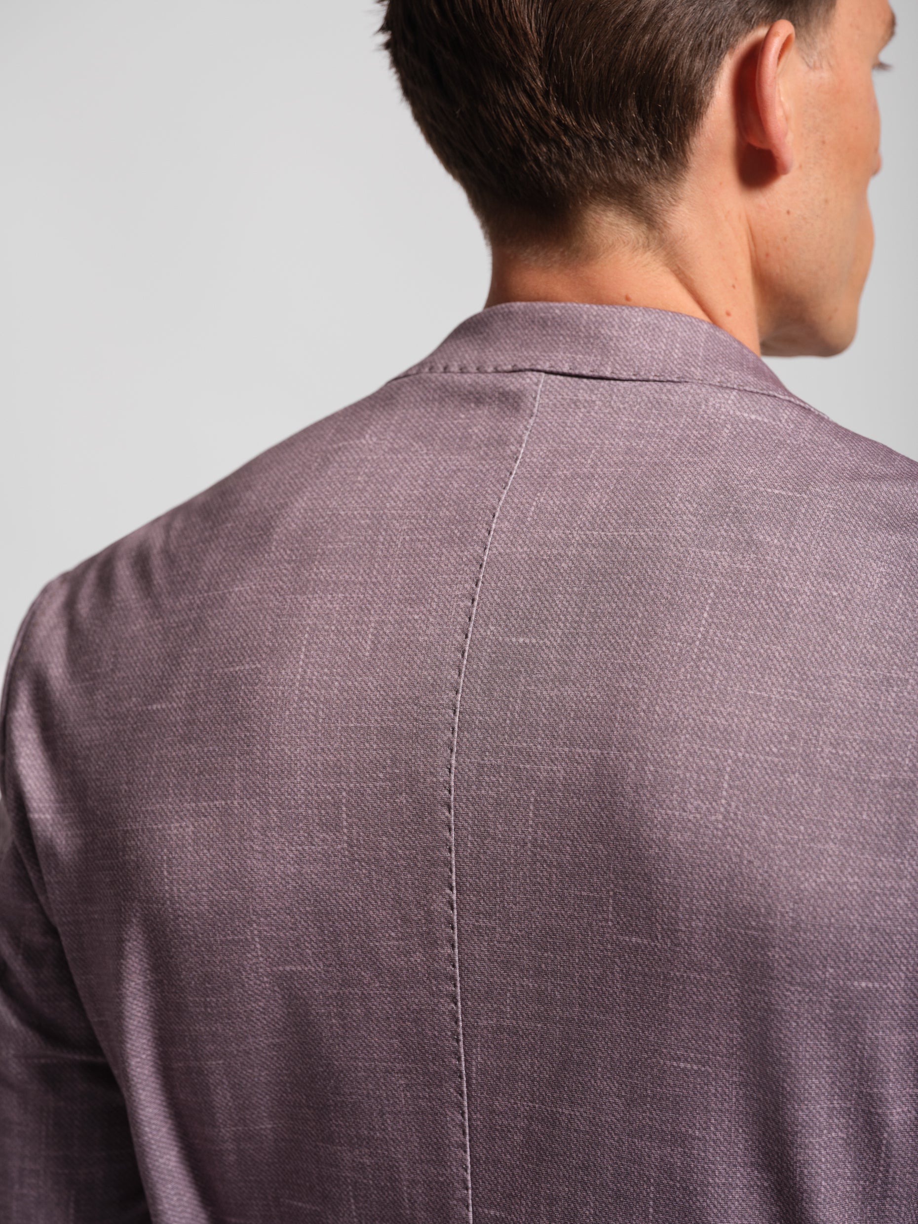 Back view of a person wearing a purple textured comfortable blazer against a light gray background