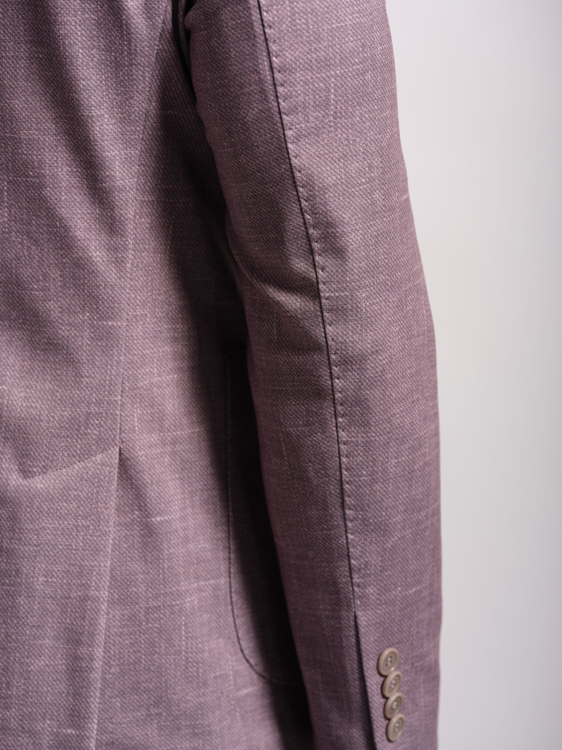 Close-up of a purple blazer with button and top sticth details on a white background
