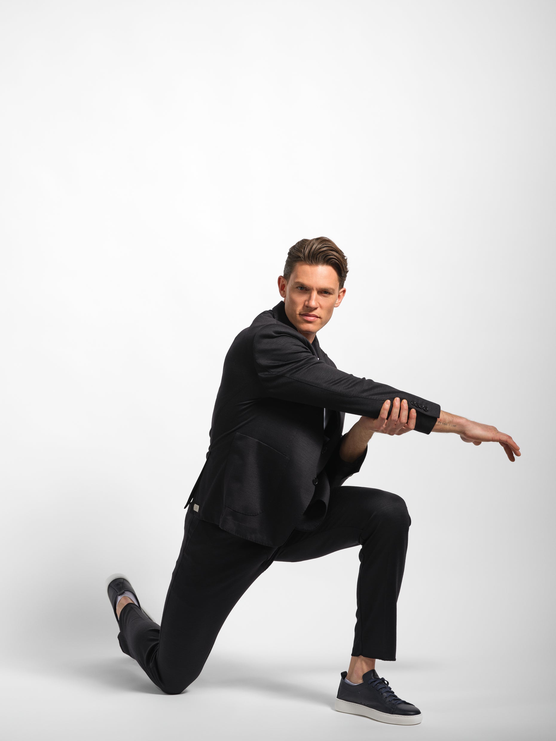 Man in a black suit posing wearing a black jersey stretch suit