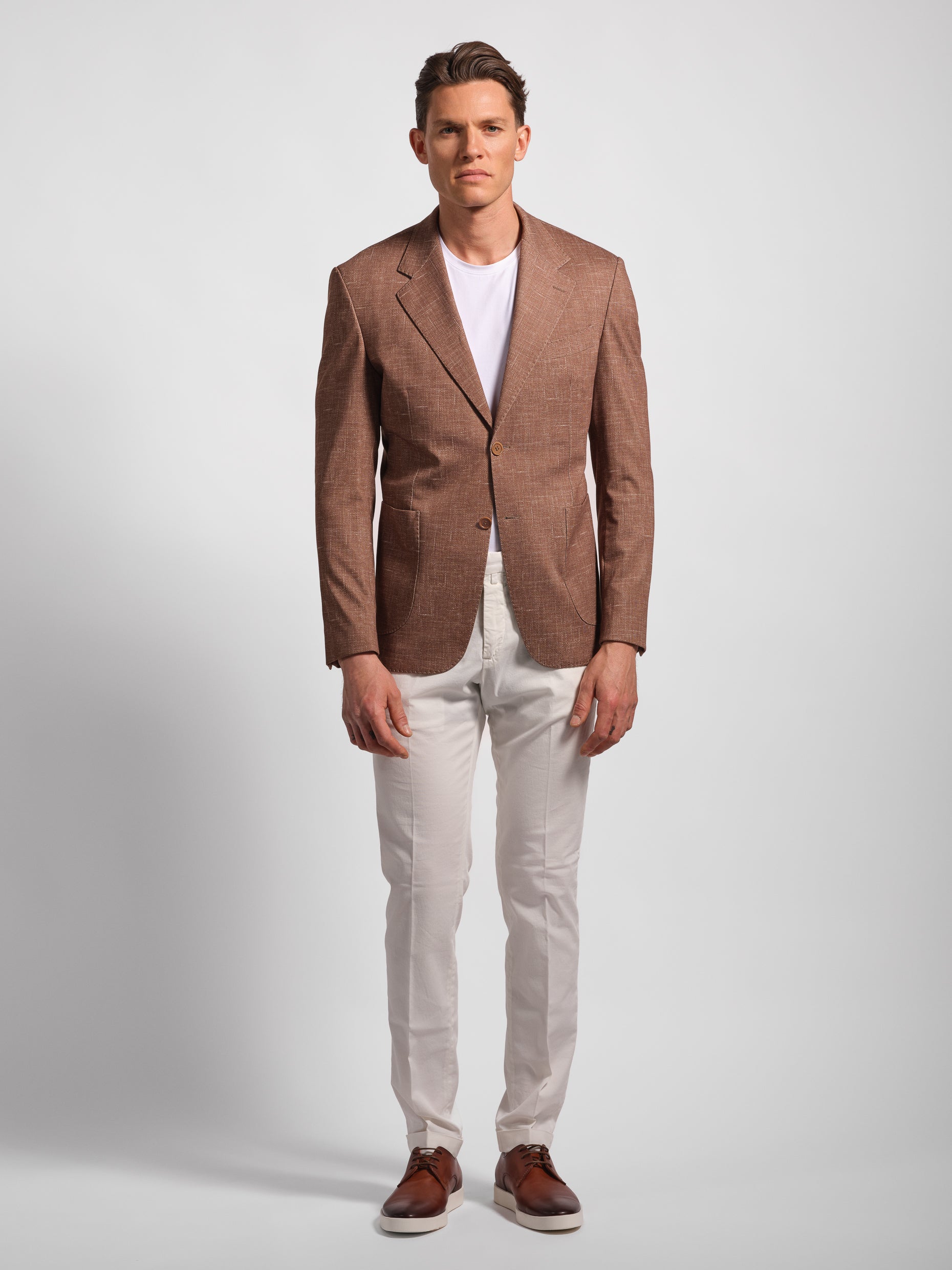 Man in a stretchy, comfortable jersey brown blazer over a white t-shirt with navy pants 2 button