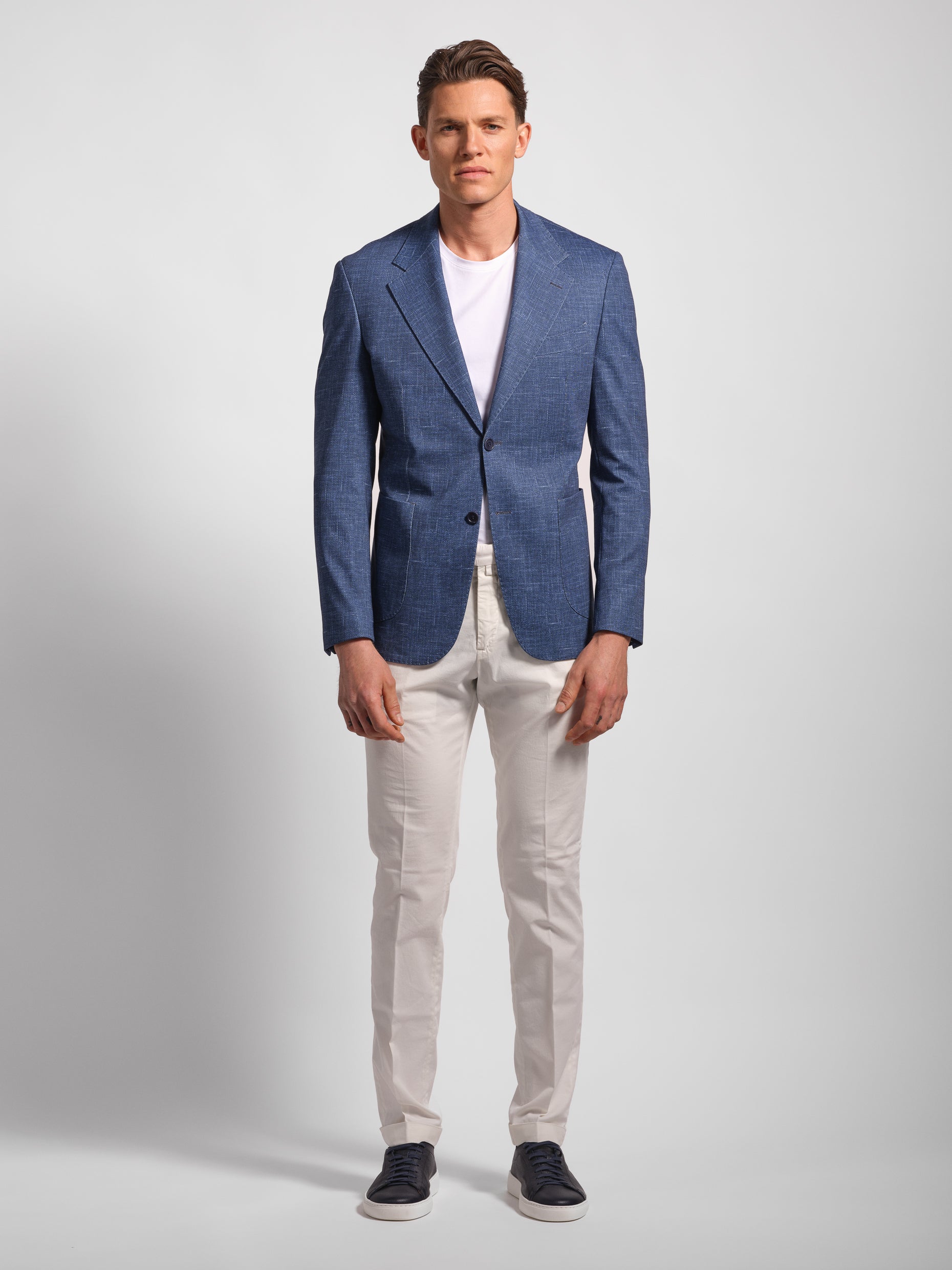 Man in a stretchy, comfortable Navy Jersey 2-button blazer jacket over a white t-shirt with navy pants wearing Man Wears Sheep with patch pockets
