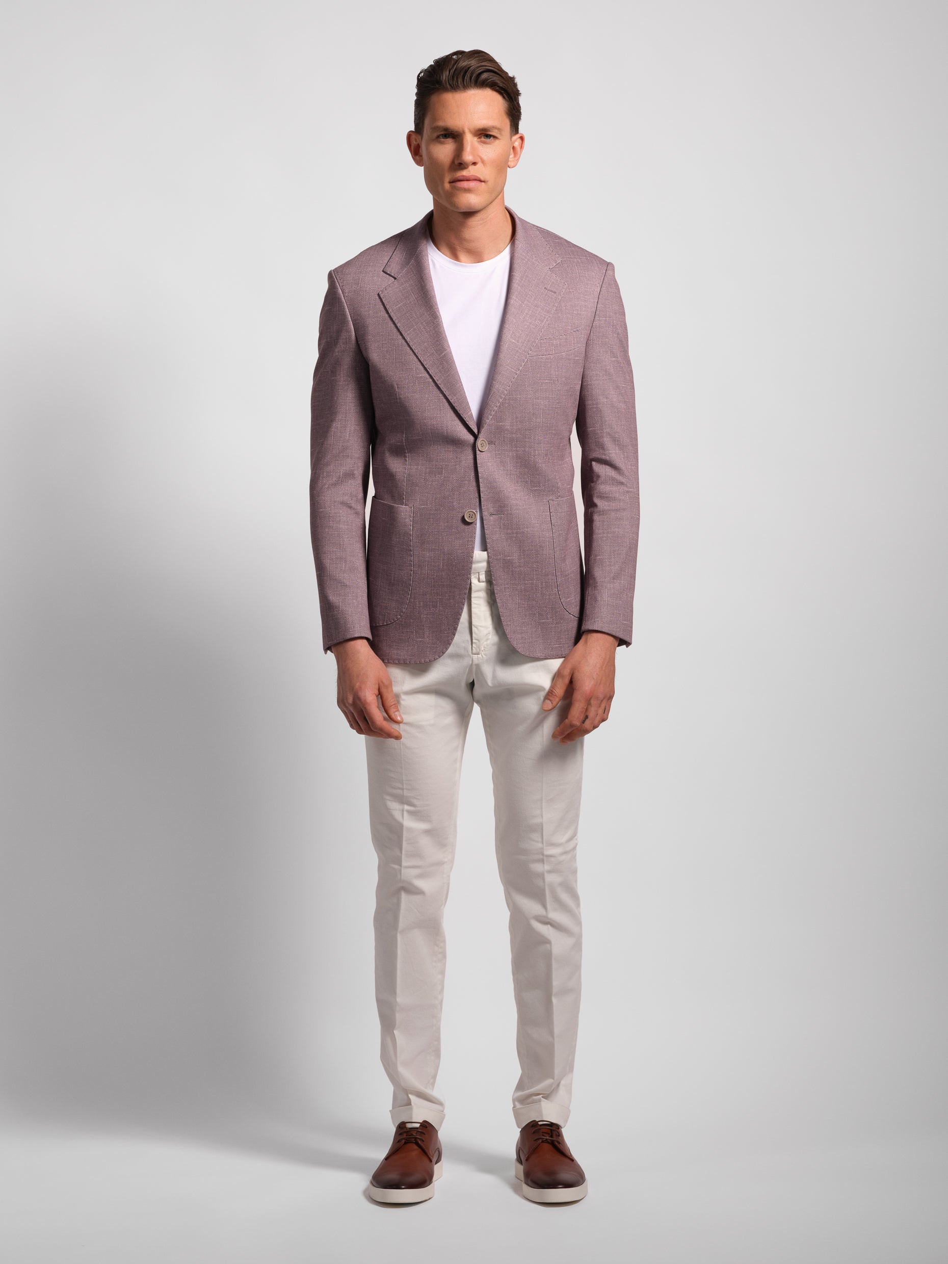 Man wearing a light purple blazer over a white shirt with white pants on a plain background