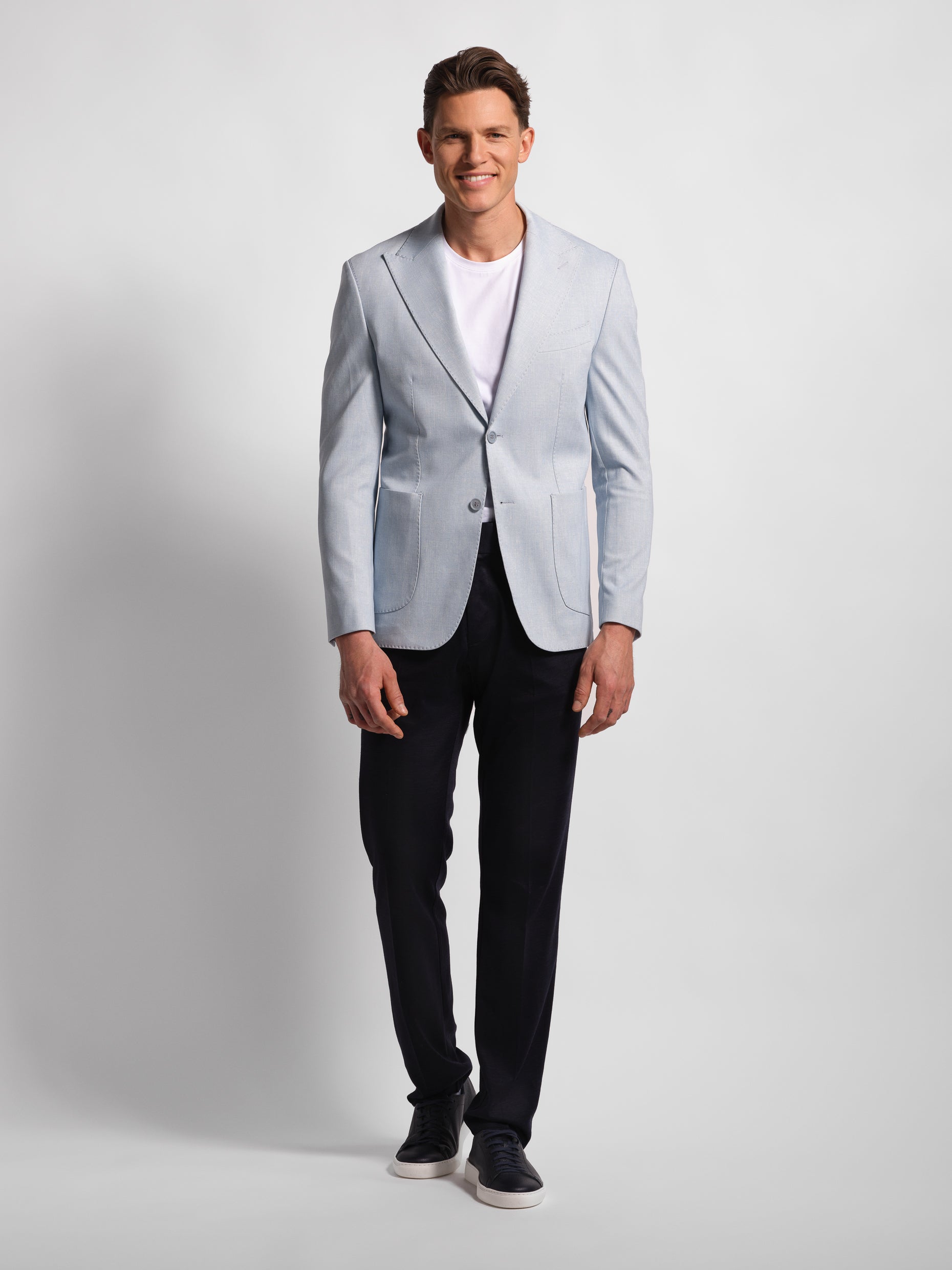 Man wearing a light blue blazer over a white t-shirt with Navy pants on a plain background
