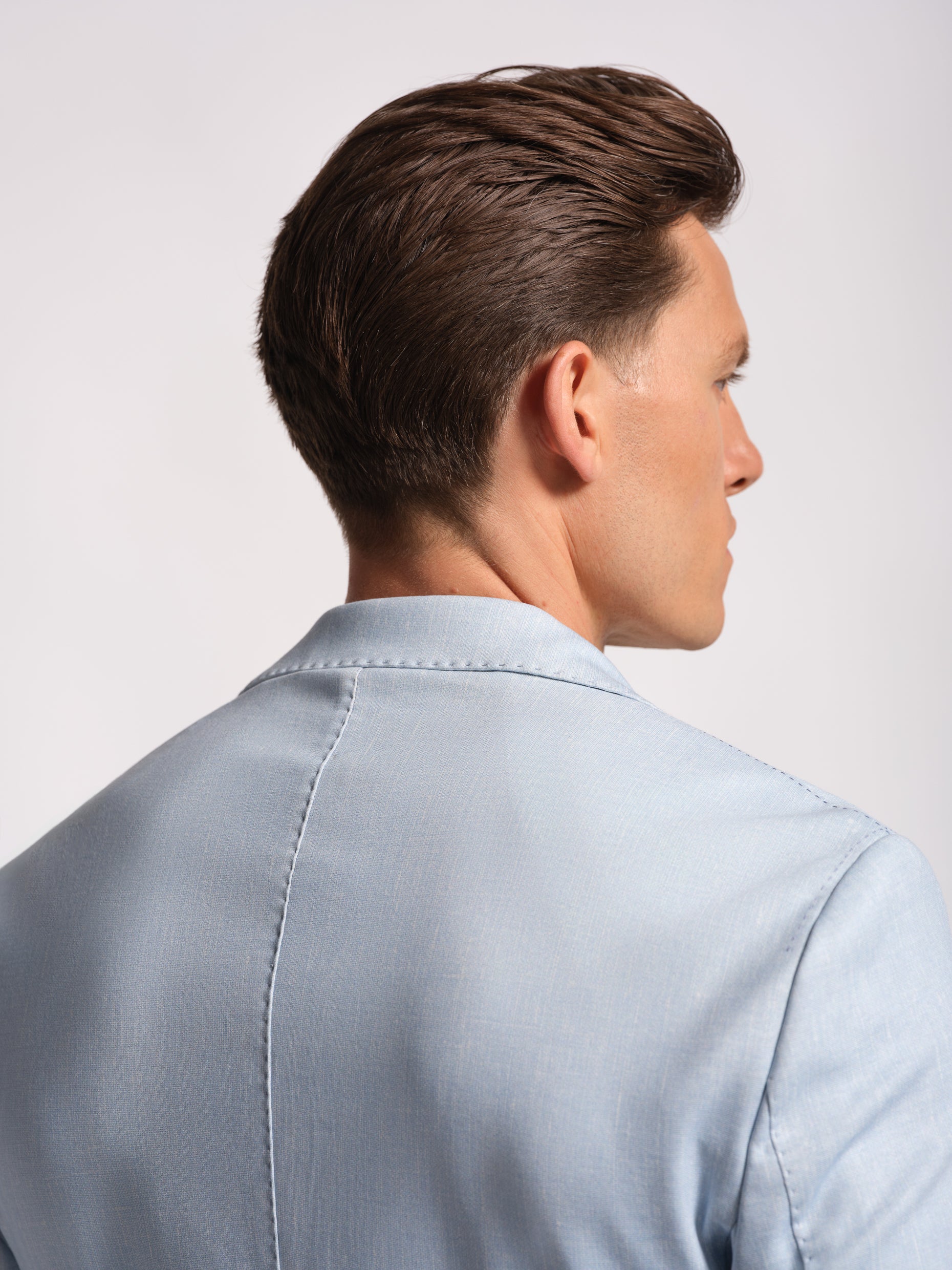 Man wearing a light blue blazer against a plain background upper back