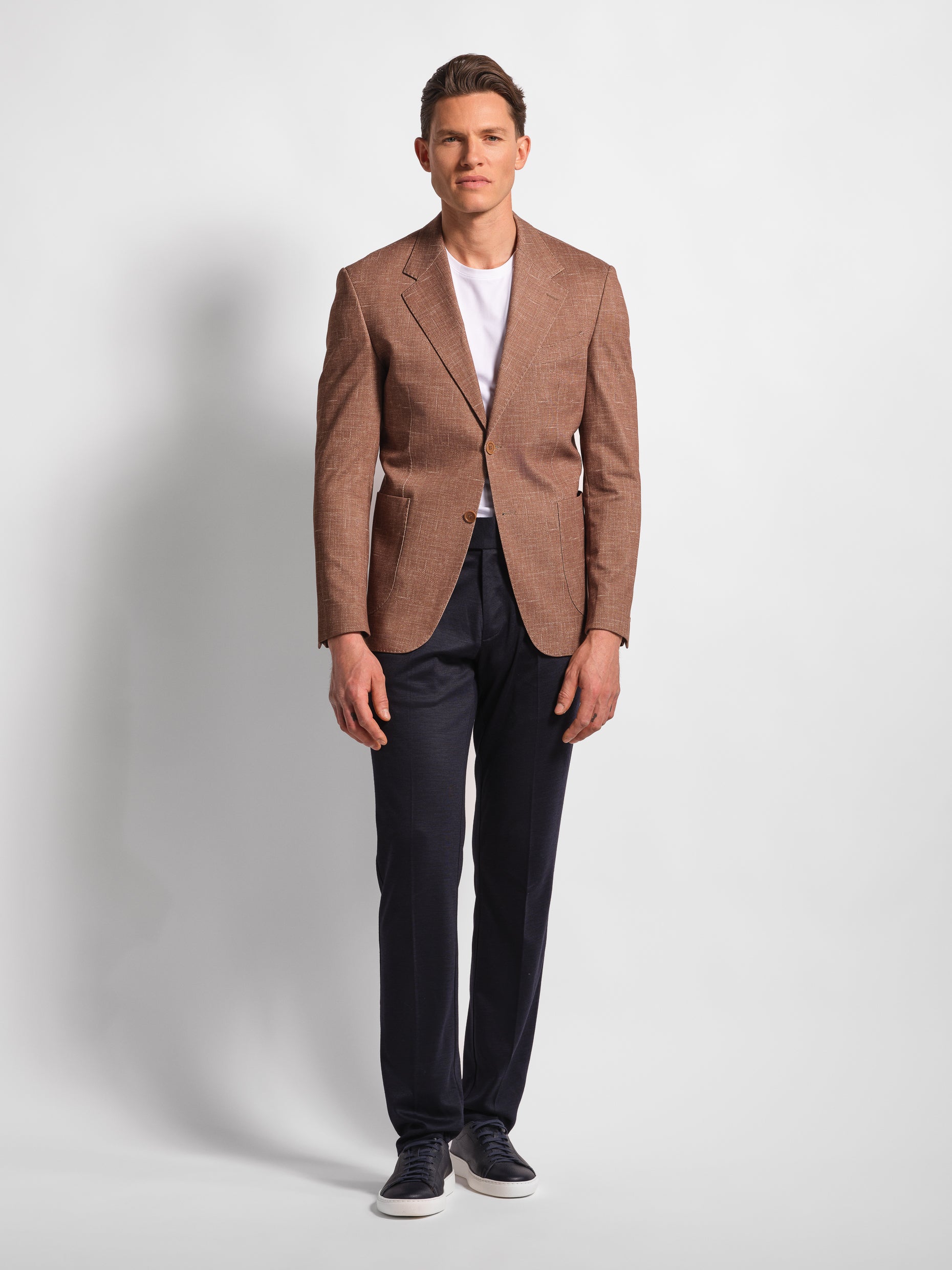 Man in a stretchy, comfortable jersey brown blazer over a white t-shirt with navy pants 