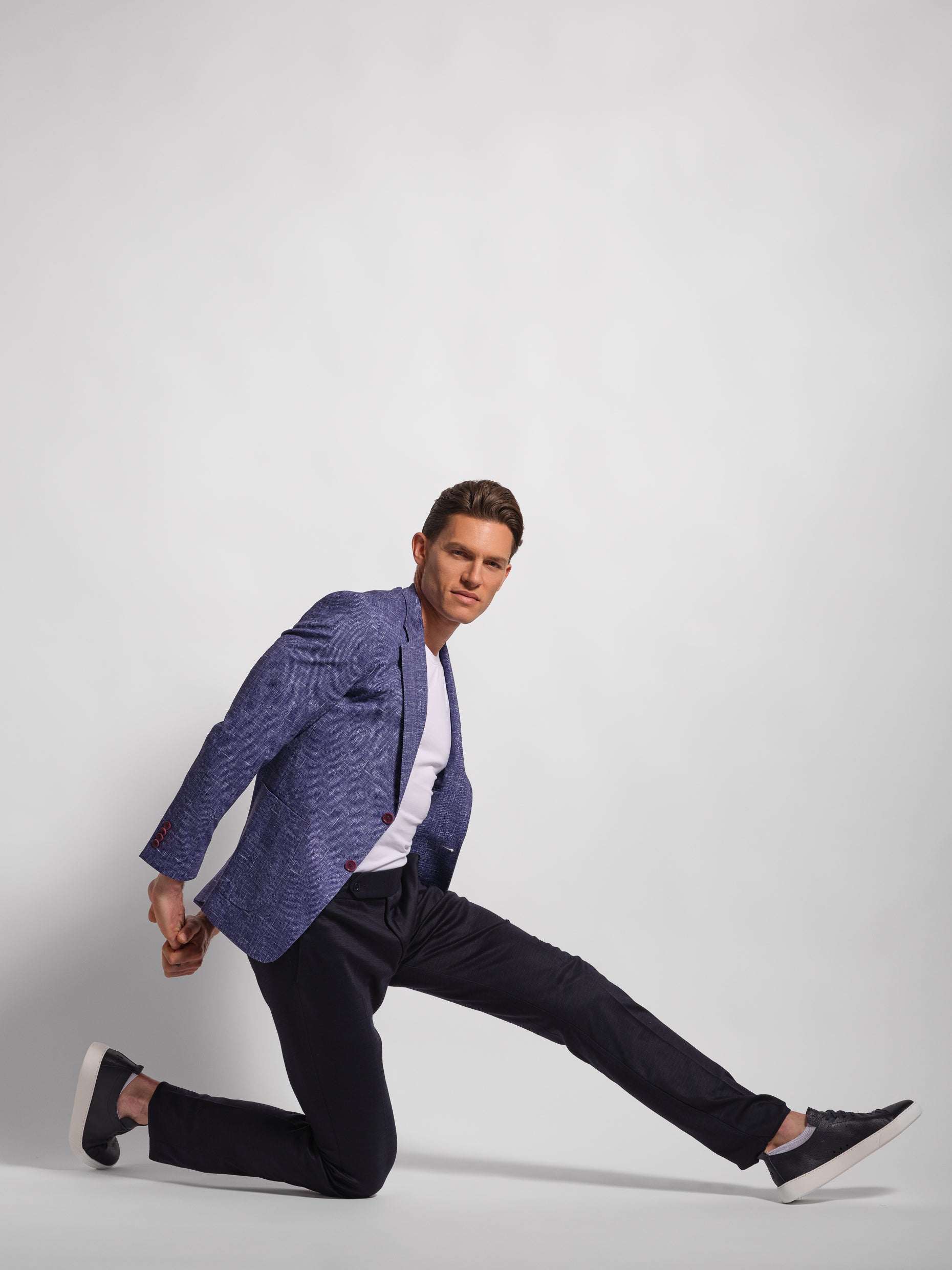 Man wearing a stretch jersey purple blazer over a white shirt and Navy pants with wide notch lapels and patch pockets model doing athletic 